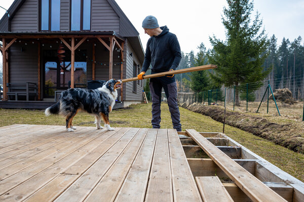 Mann arbeitet an einer Terrassenplattform mit seinem treuen Hund im Garten eines Landhauses
